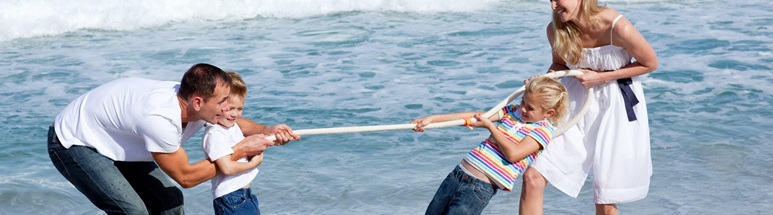 Mutter, Vater und zwei Kinder spielen Tauziehen am Strand