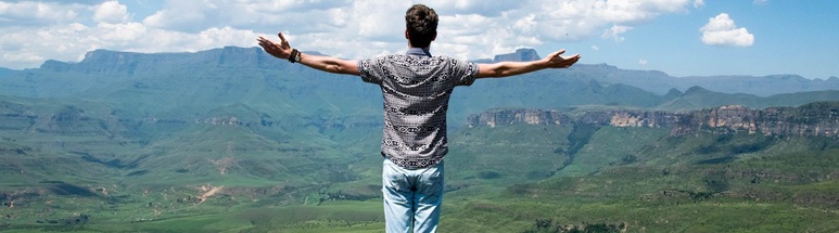 Mann steht mit ausgebreiteten Armen auf einem Berggipfel