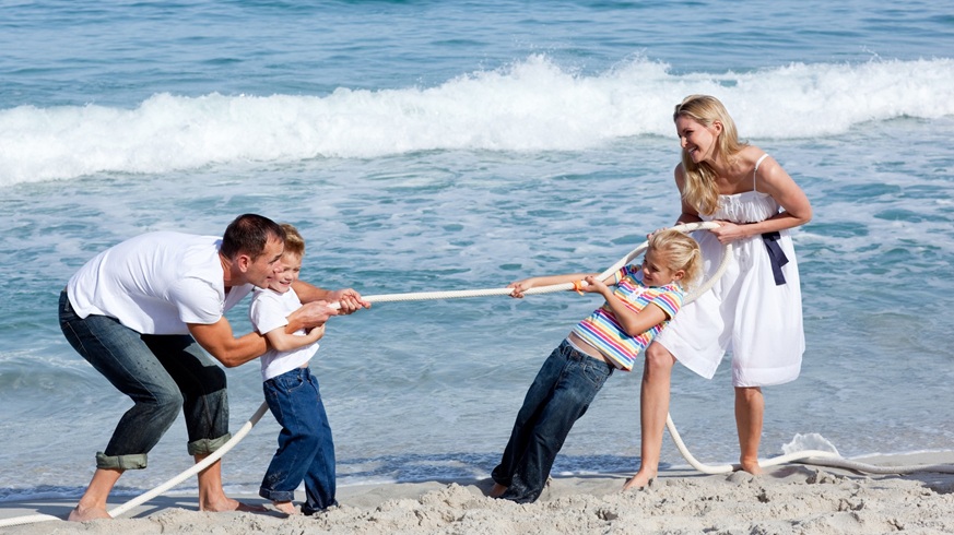 Mutter, Vater und zwei Kinder spielen Tauziehen am Strand