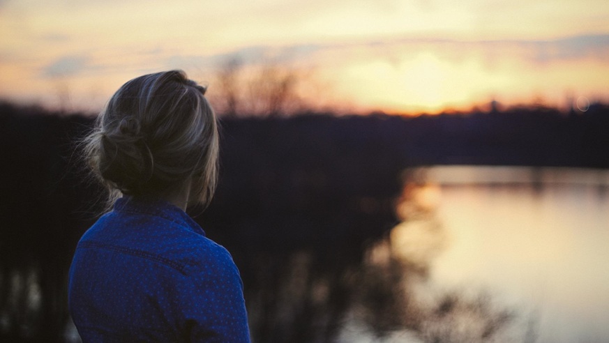 Frau von hinten schaut auf einen See bei Sonnenuntergang