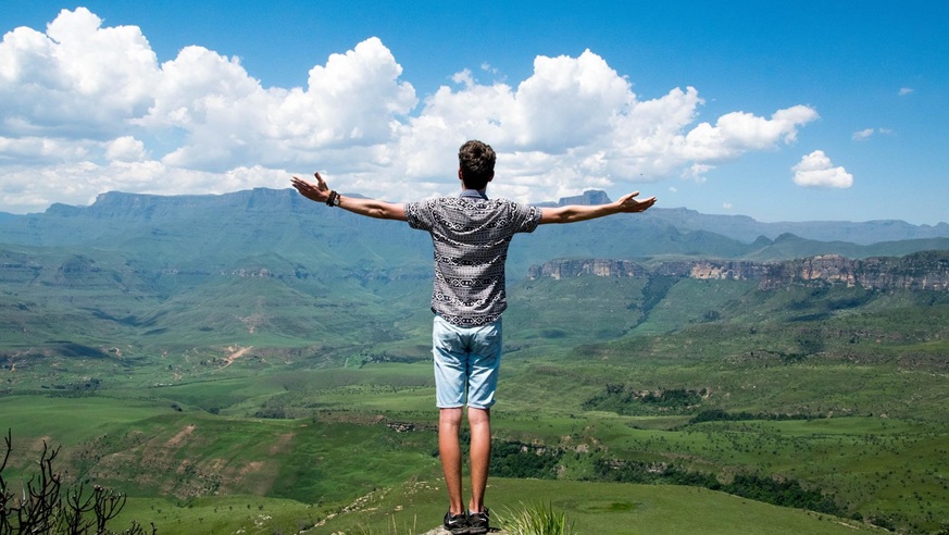 Mann steht mit ausgebreiteten Armen auf einem Berggipfel